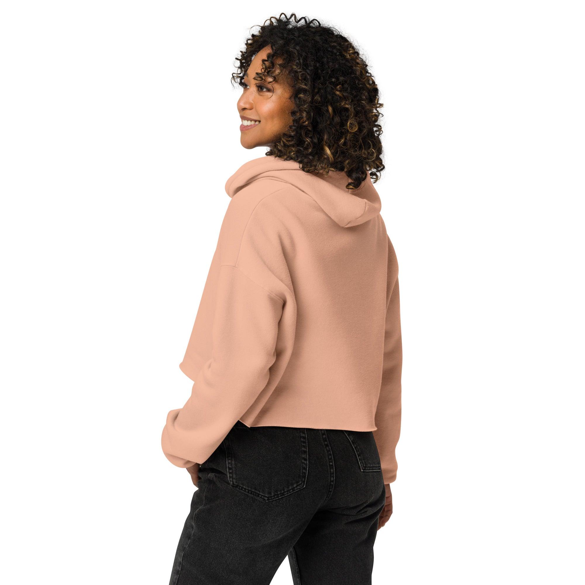 Frau trägt rosa Cropped-Hoodie und schwarze Jeans vor weißem Hintergrund