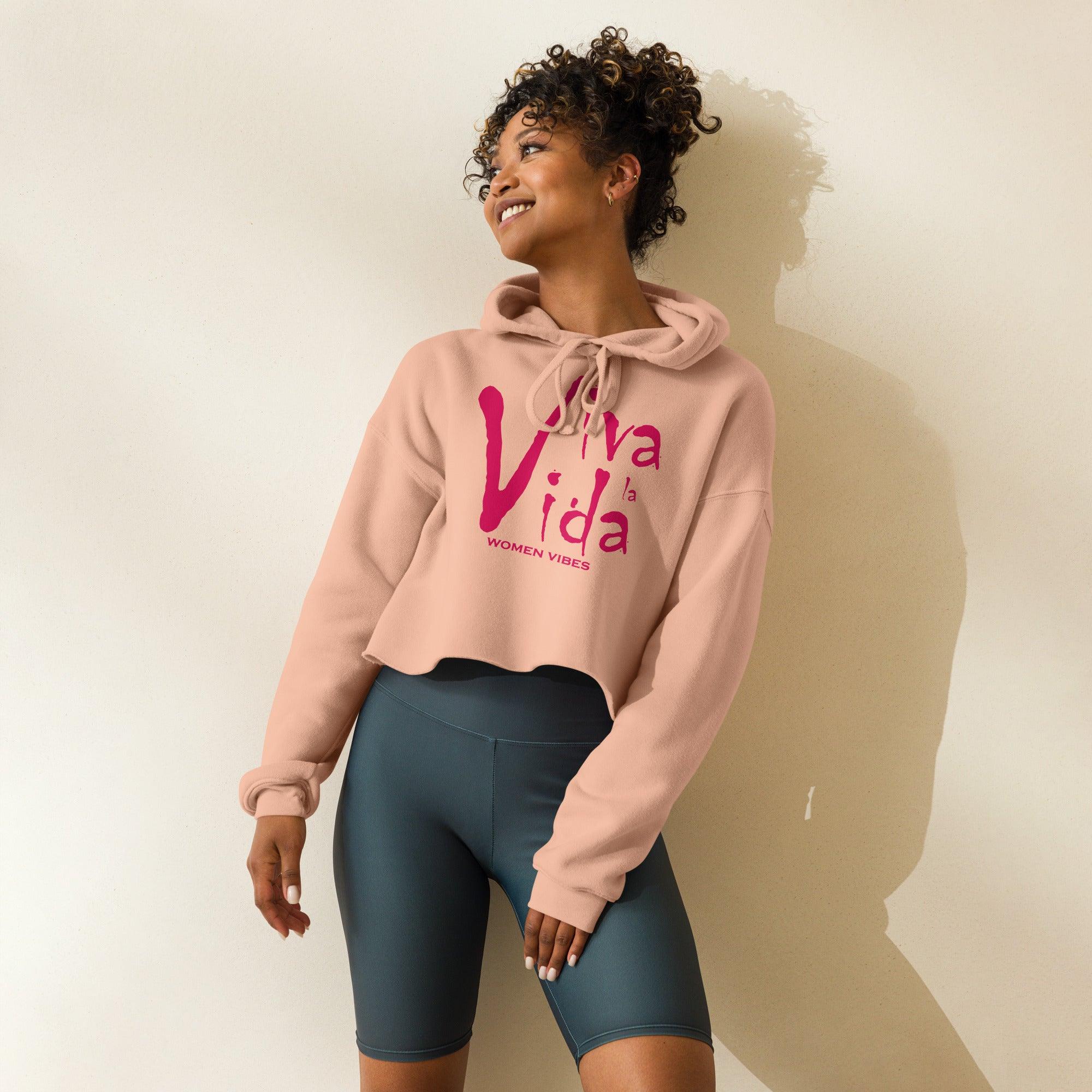 Frau trägt rosa Crop-Hoodie mit Viva la Vida Print und dunkelgrauer Radlerhose, sportliche Mode
