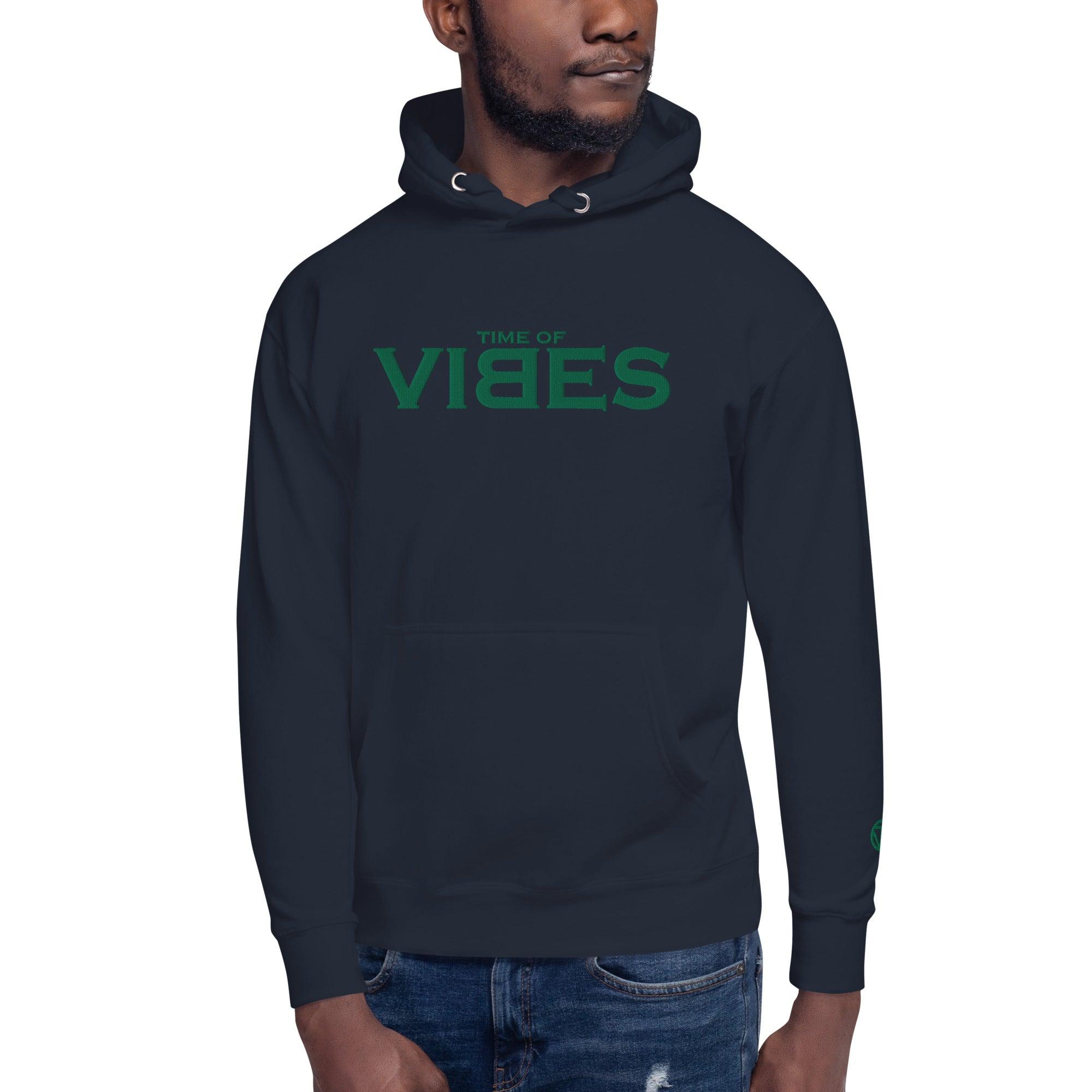 Mann trägt dunkelblauen VIBES Hoodie mit grüner Stickerei und Kängurutasche