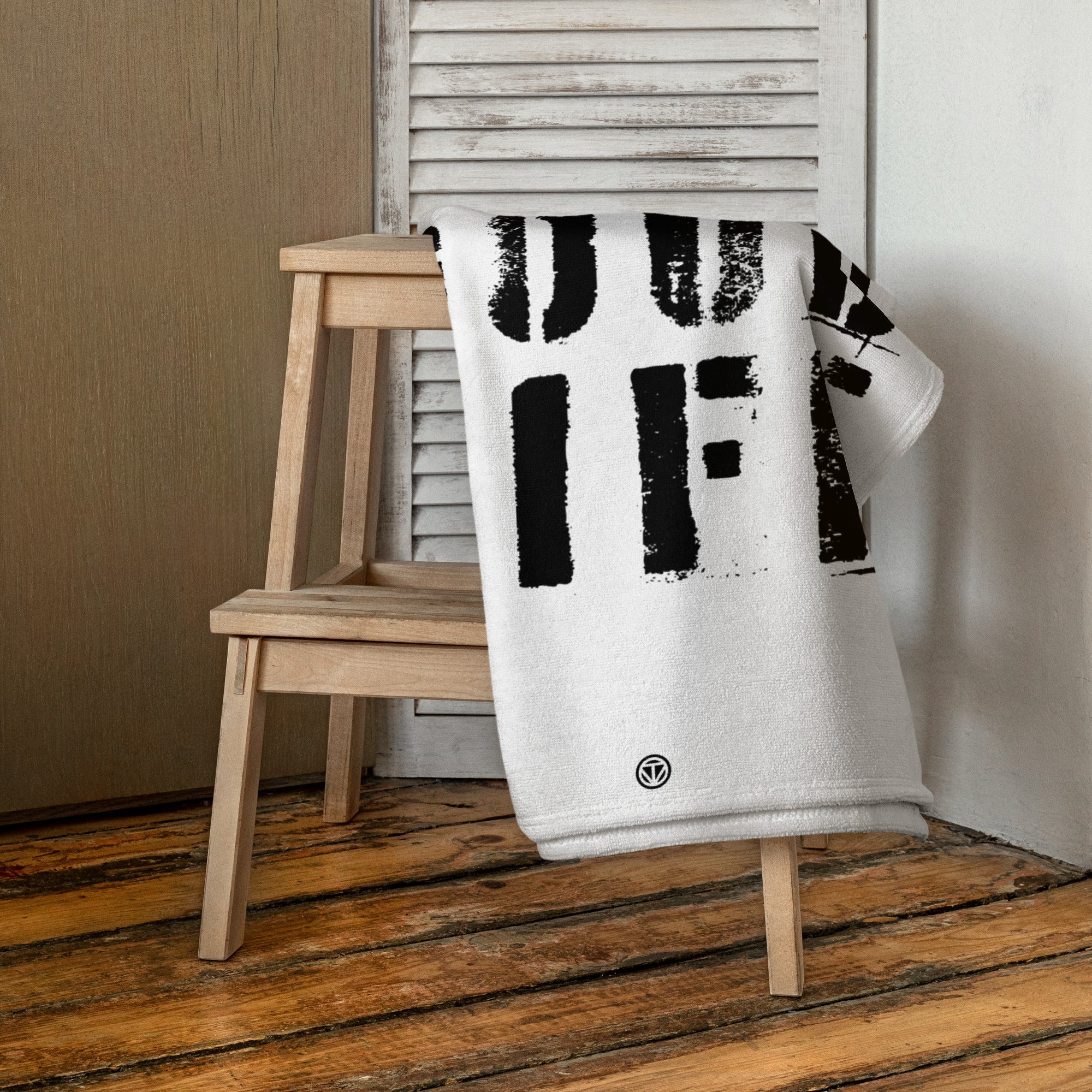 Weißes Strandtuch mit schwarzem Schriftzug auf Holzstuhl vor weißer Jalousie in modernem Raum