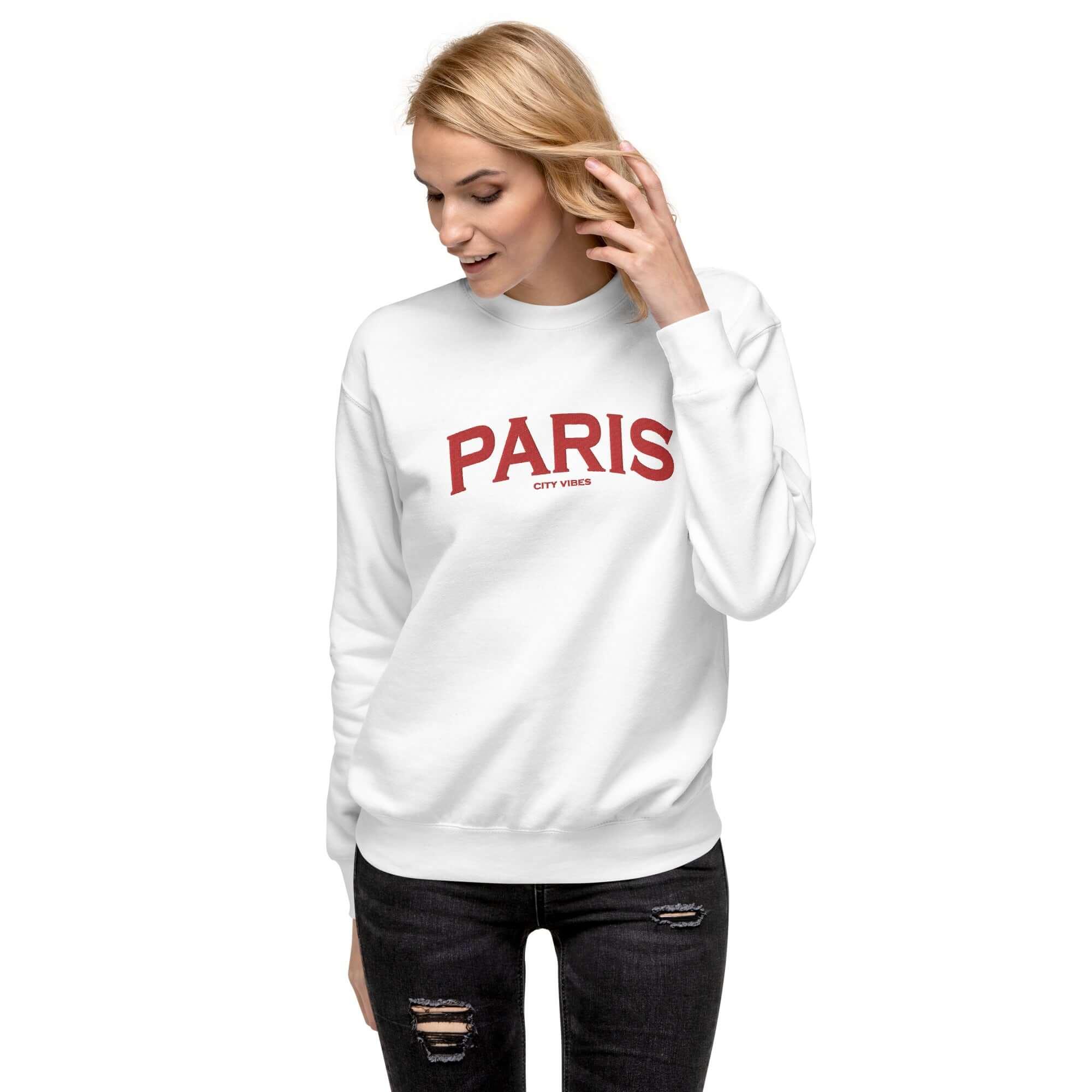 Frau trägt weißen Unisex-Sweatshirt mit rotem Paris-Schriftzug, schwarze Jeans