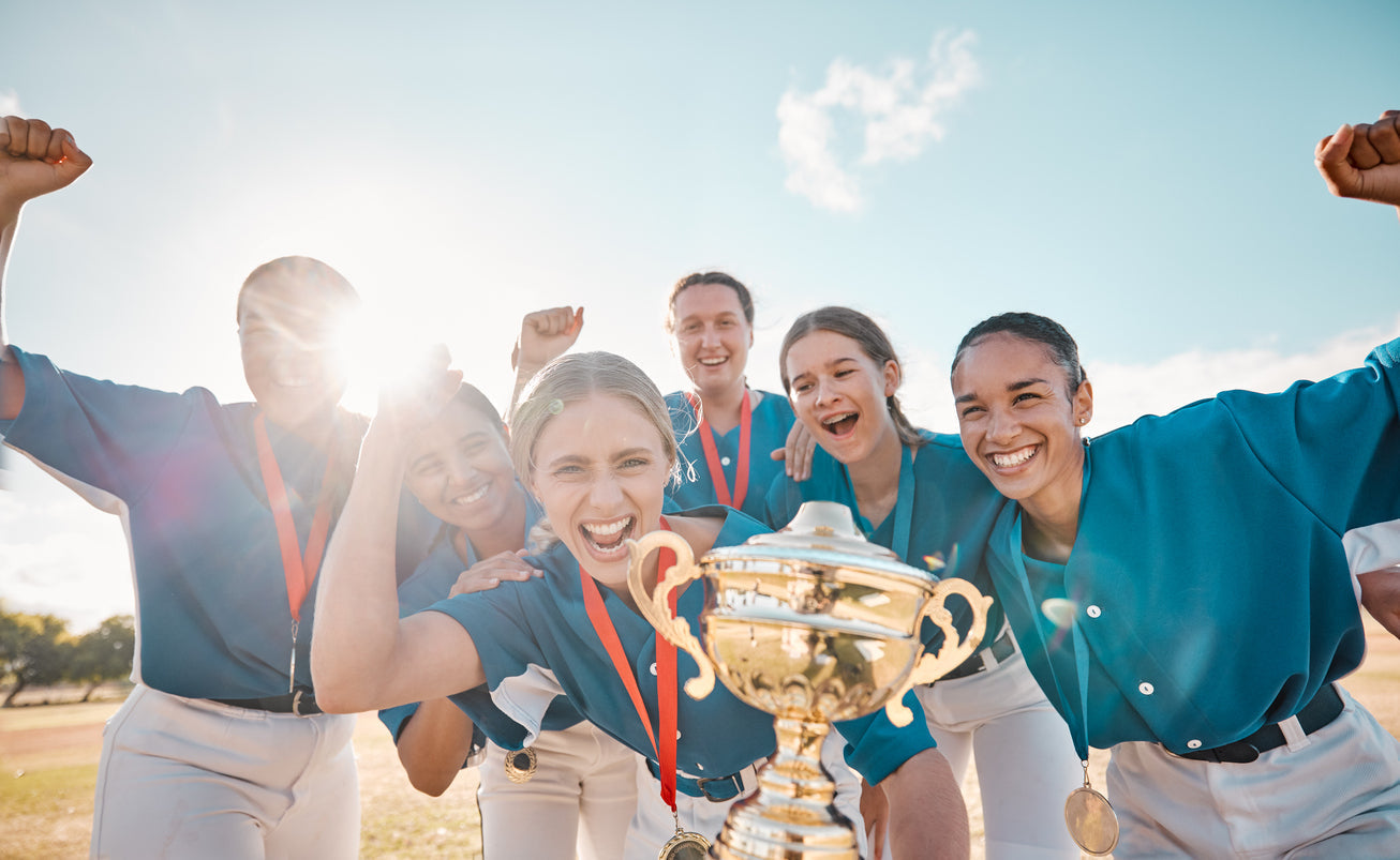 Jubelndes Damen-Team in blauer Vereinskleidung mit Pokal und Medaillen auf dem Sportplatz