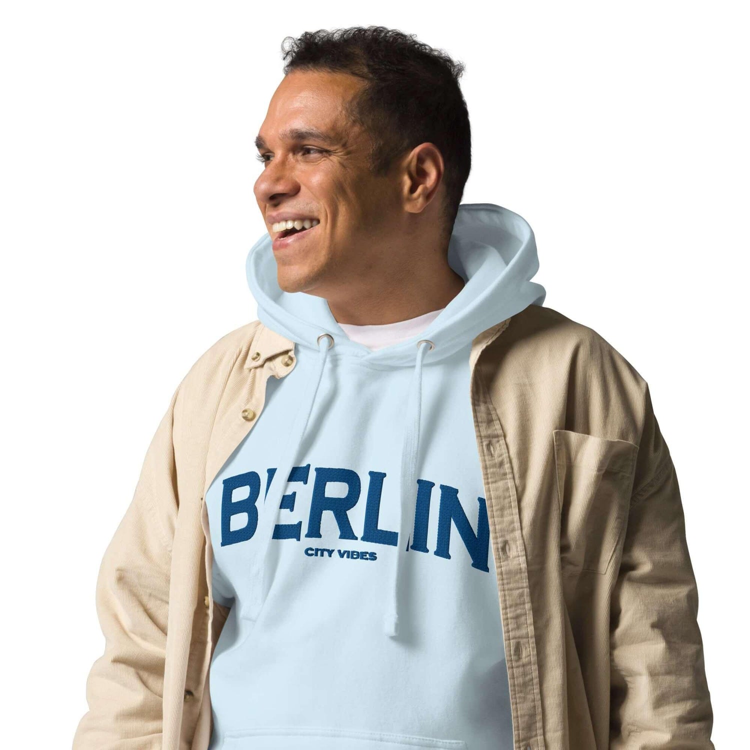 Mann trägt hellblauen Berlin Hoodie und beiges Hemd, vor weißem Hintergrund