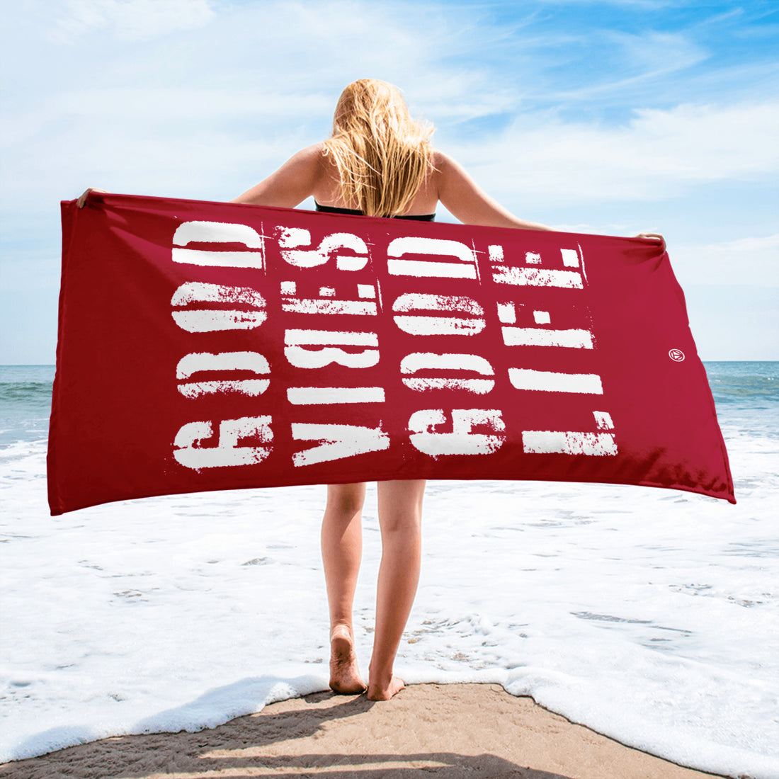 Frau am Strand hält rotes Strandtuch mit weißem Schriftzug &