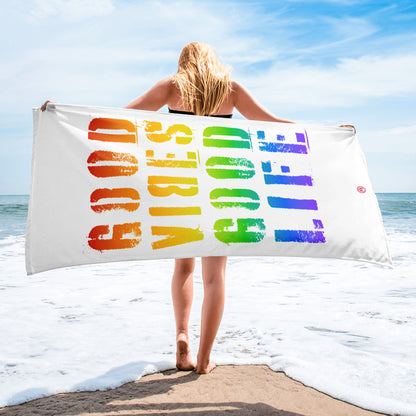 Frau am Strand mit weißem Strandtuch, farbiger Regenbogen-Print "Good Vibes Good Life" bei sonnigem Wetter