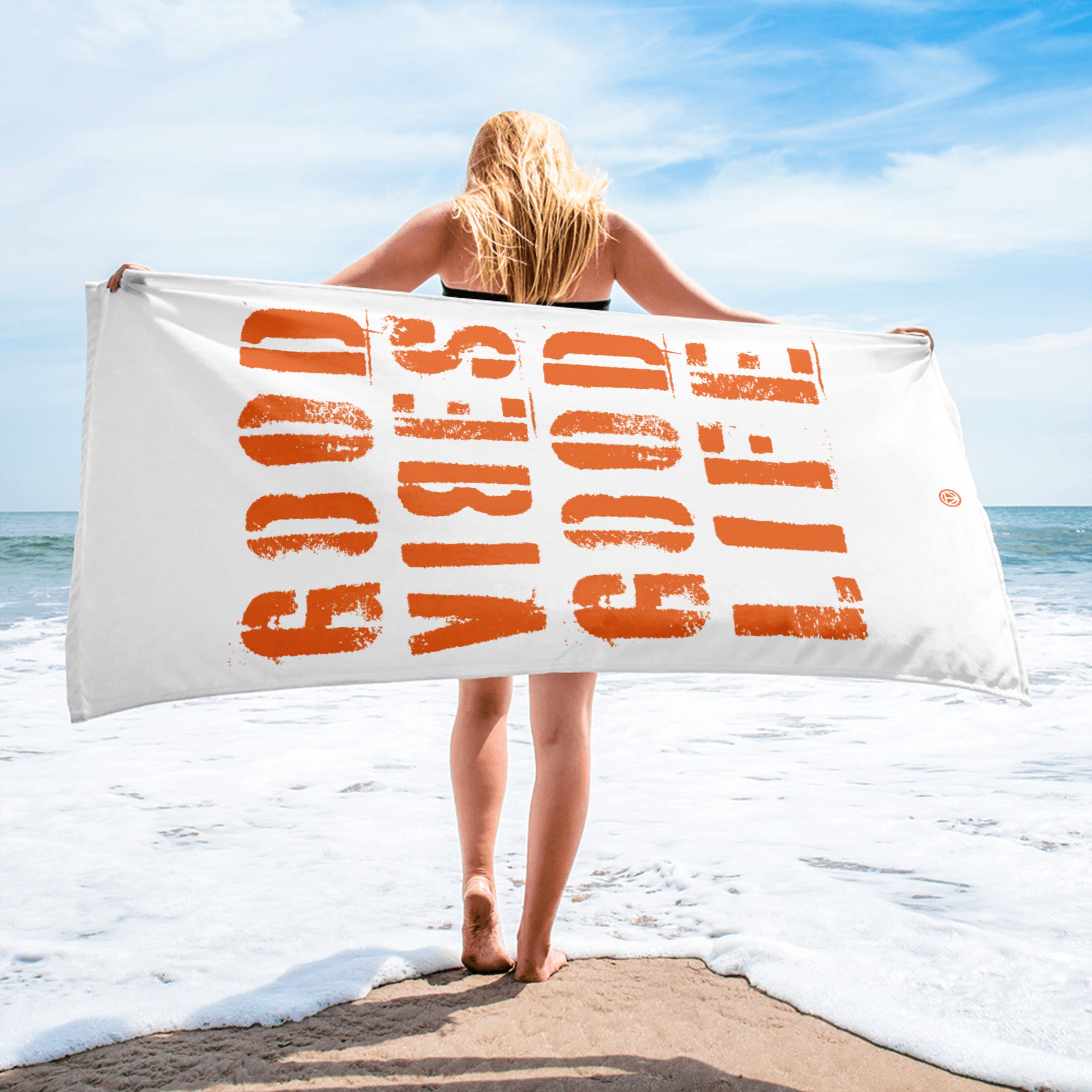 Frau am Strand hält weißes Strandtuch mit orangefarbenem Schriftzug &
