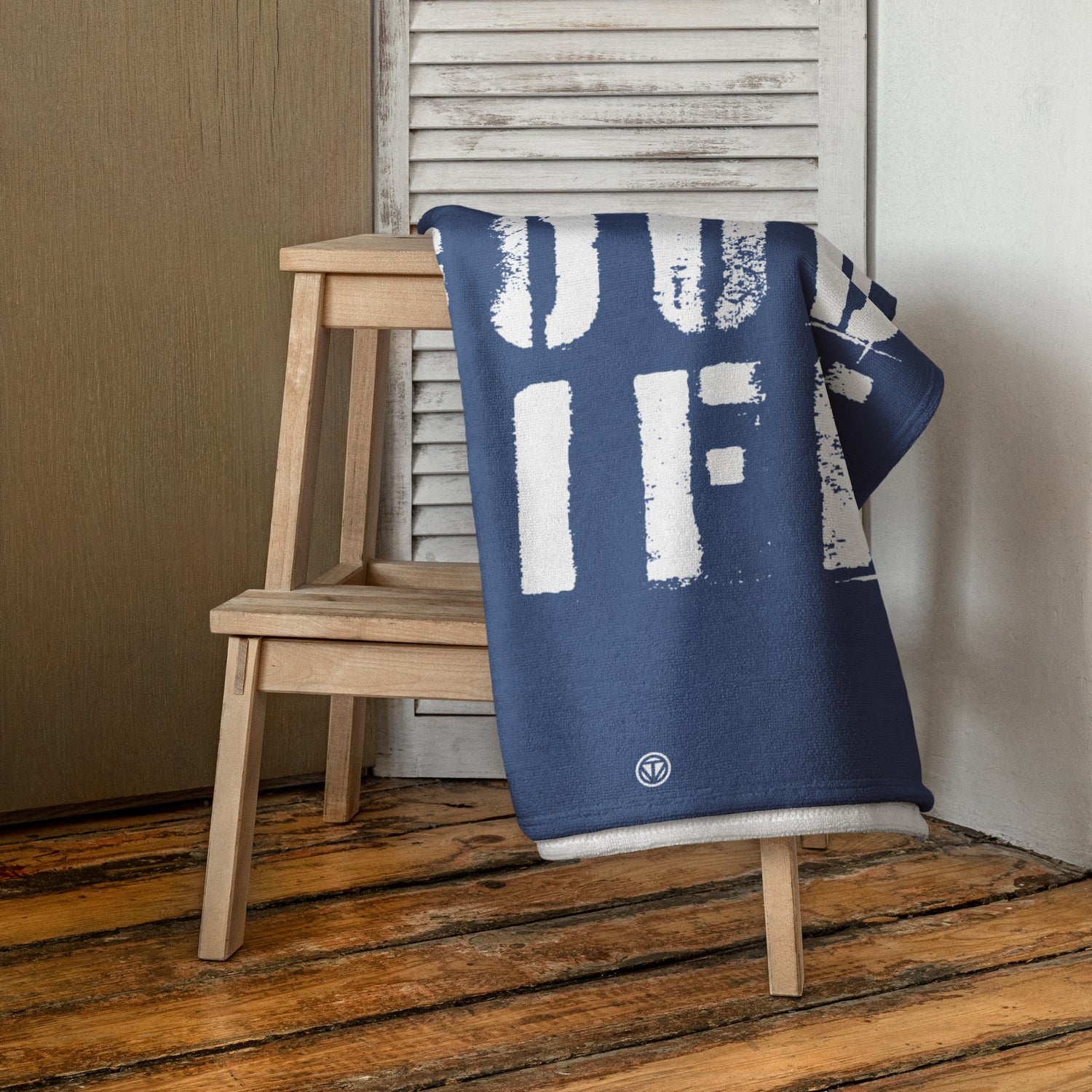 Blau weißes Strandtuch mit großem Schrift-Design auf Holzstuhl vor weißem Fensterladen im Raum