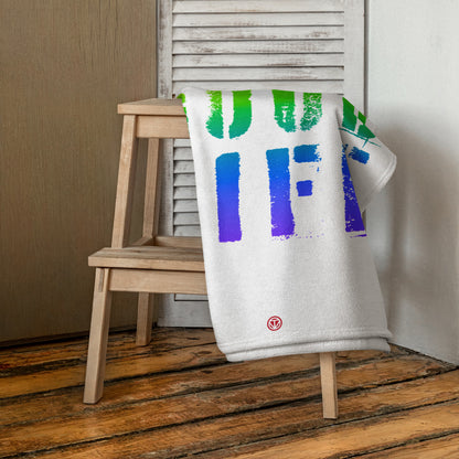 Weiße Strandtuch mit buntem Schrift-Design über hölzernem Hocker vor weißem Fensterladen im Raum