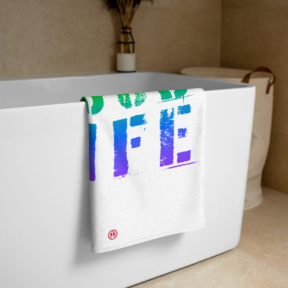 Weißes Badetuch mit buntem Farbverlauf-Design hängt an moderner weißer Badewanne in hellem Badezimmer